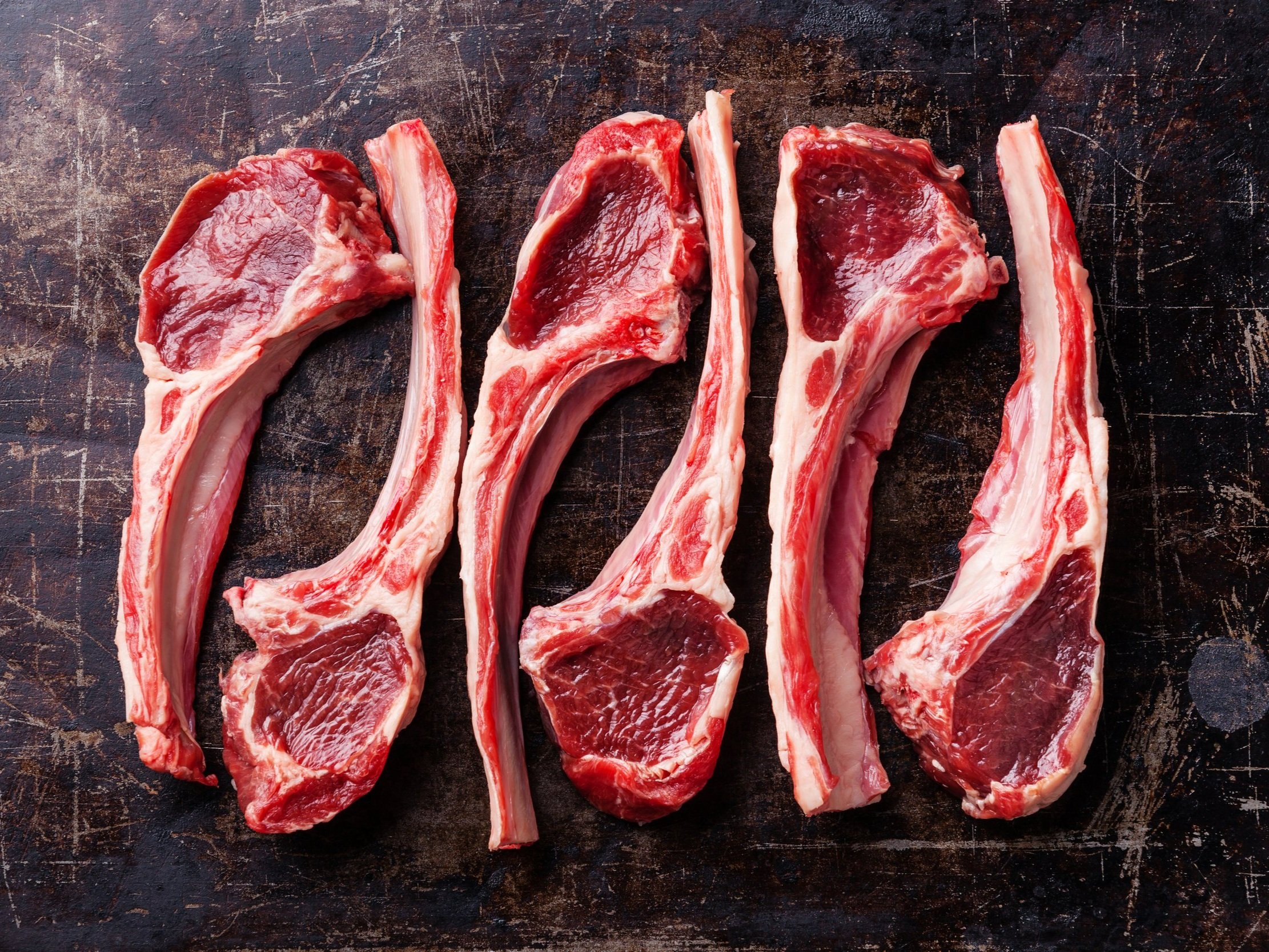 Fresh, uncooked lamb chops arranged on a rustic wooden surface, showcasing their rich red color and marbling, ideal for grilling or roasting.